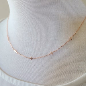 Puede incluir: Un delicado collar de oro rosa con pequeños dijes de cruz. El collar se muestra sobre un fondo blanco, resaltando la fina cadena y las cruces espaciadas uniformemente. La joya es simple y elegante.