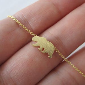 May include: A gold chain necklace with a bear silhouette pendant. The chain is delicate and the bear is simple and modern.