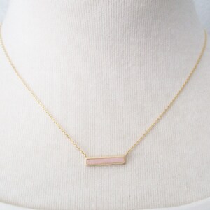 May include: A gold chain necklace with a pink rectangular pendant.
