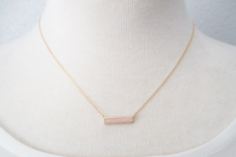 May include: A gold chain necklace with a pink rectangular pendant.