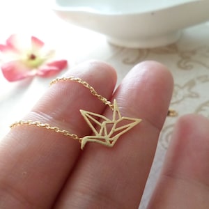 May include: A gold chain necklace with a delicate origami crane pendant. The crane is made of thin metal and has a geometric design.