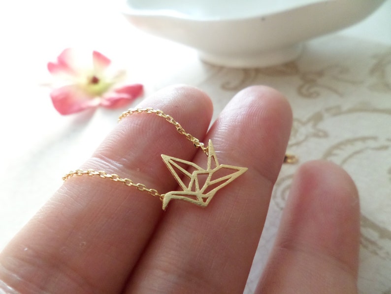 May include: A gold chain necklace with a delicate origami crane pendant. The crane is made of thin metal and has a geometric design.