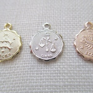 May include: Three small, round zodiac charms. One is gold with the Pisces symbol, another is silver with the Libra symbol, and the third is rose gold with the Scorpio symbol. Each charm has a scalloped edge and a small loop for attaching to a chain.