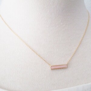 May include: A delicate gold chain necklace with a pink bar pendant.
