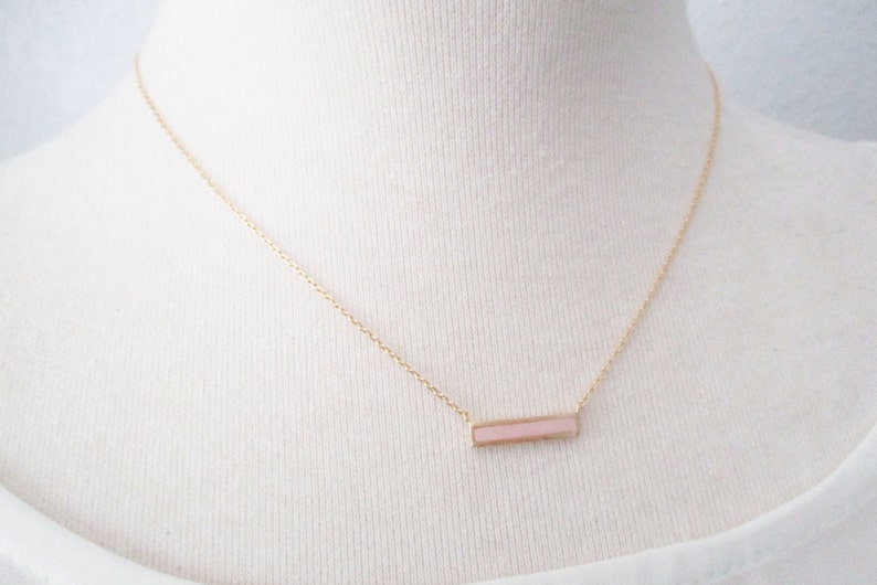 May include: A delicate gold chain necklace with a pink bar pendant.