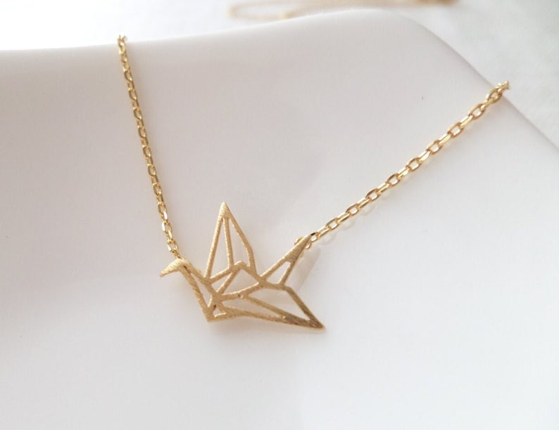 May include: A gold origami crane necklace with a delicate chain. The crane is a symbol of peace and good luck.