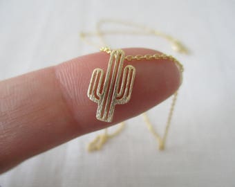 May include: A gold chain necklace with a delicate cactus pendant. The pendant is a simple outline of a cactus with multiple arms.