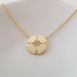 May include: A gold necklace with a compass pendant. The compass has a star in the center and the letters N, S, E, and W around the edge.