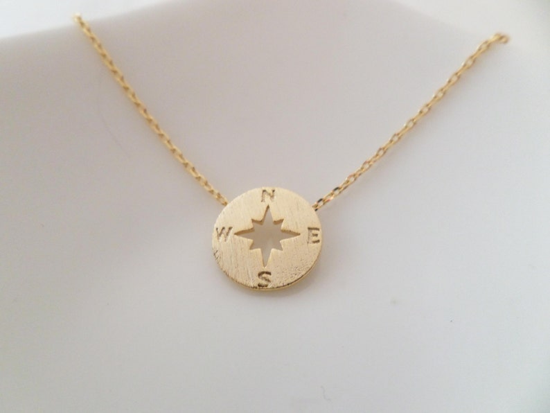 May include: A gold necklace with a compass pendant. The compass has a star in the center and the letters N, S, E, and W around the edge.
