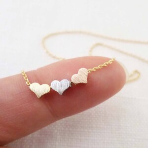 May include: A gold chain necklace with three small heart charms. The hearts are different colors: gold, silver, and rose gold.