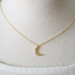 May include: A gold chain necklace with a crescent moon pendant encrusted with small clear stones.