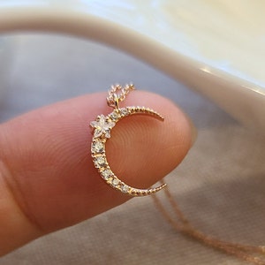 May include: A gold crescent moon necklace with a small star charm, adorned with sparkling clear cubic zirconia stones.