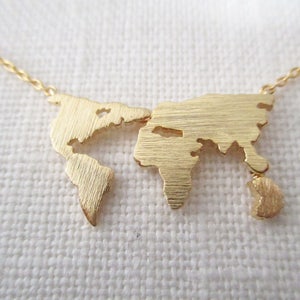 May include: A gold necklace featuring a world map pendant. The pendant is crafted from brushed metal and has a textured finish.