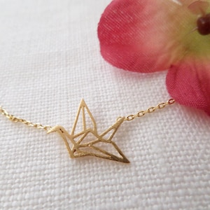 May include: A gold chain necklace with a delicate origami crane pendant. The crane is made of thin metal and has a detailed design.