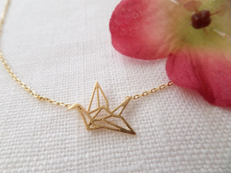 May include: A gold chain necklace with a delicate origami crane pendant. The crane is made of thin metal and has a detailed design.
