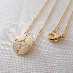 May include: A gold compass necklace with a delicate chain. The compass pendant features a cut-out star design and the letters N, S, E, and W.