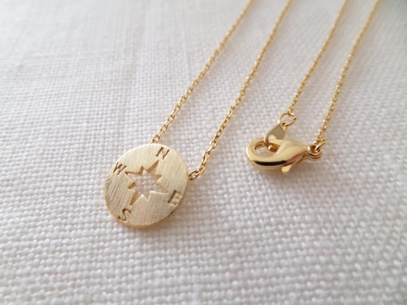 May include: A gold compass necklace with a delicate chain. The compass pendant features a cut-out star design and the letters N, S, E, and W.