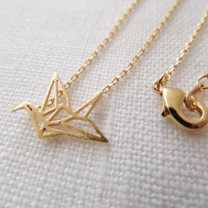 May include: A gold chain necklace with a delicate origami crane pendant. The chain is a simple, linked style and the crane is a cutout design.