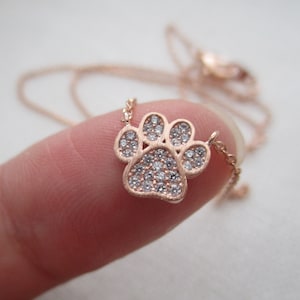 May include: Rose gold paw print pendant necklace with clear crystal accents. The necklace features a delicate chain and a detailed paw print charm, perfect for pet lovers.
