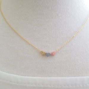 May include: A gold chain necklace with three small heart charms. The hearts are different colors: gold, silver, and pink.