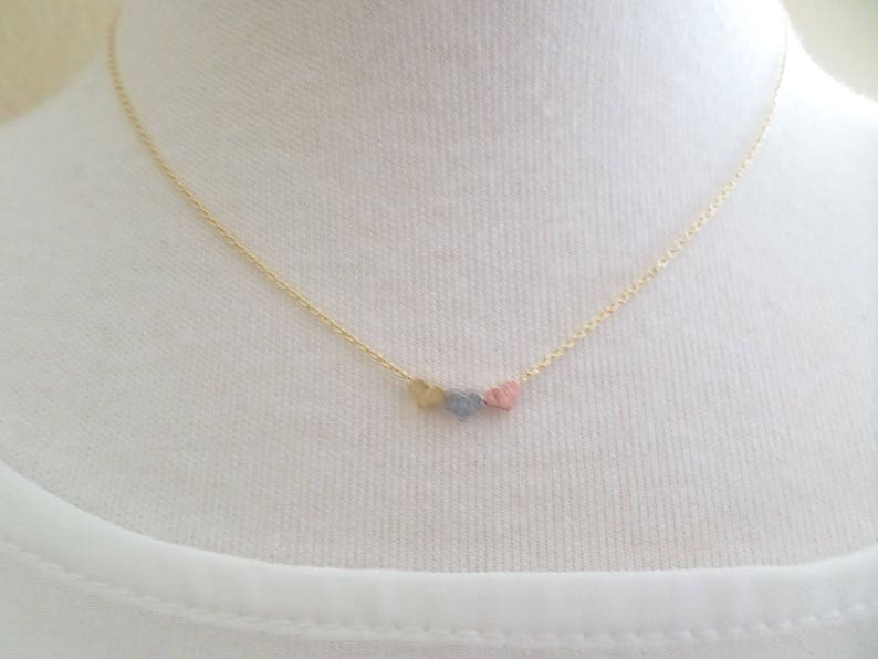 May include: A gold chain necklace with three small heart charms. The hearts are different colors: gold, silver, and pink.