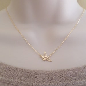 May include: A gold chain necklace with a delicate origami crane pendant.