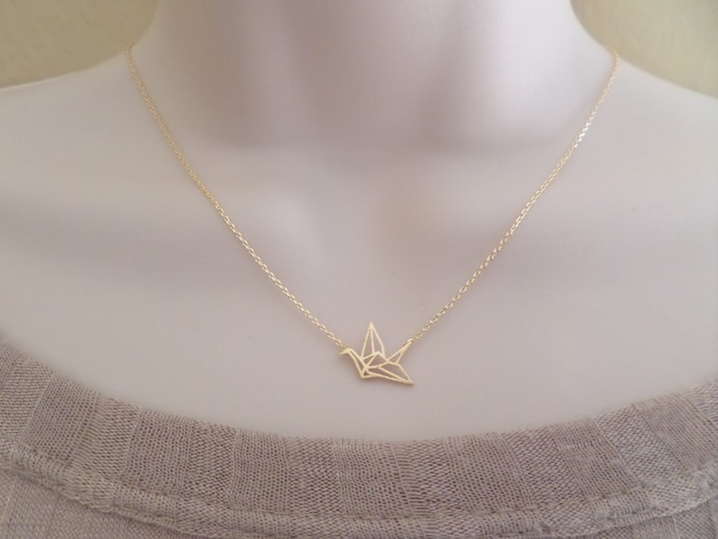 May include: A gold chain necklace with a delicate origami crane pendant.
