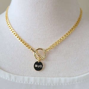 May include: A gold chain necklace with a toggle clasp and a round pendant with the initials "M♥B" engraved on it.