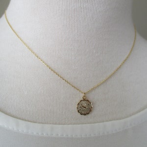 May include: Gold-toned necklace with a small, round pendant. The pendant features a detailed zodiac symbol, likely a scorpion, within a decorative frame. The chain is delicate, and the necklace is displayed on a white background.