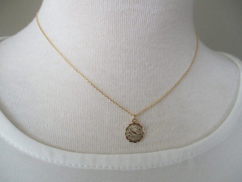 May include: Gold-toned necklace with a small, round pendant. The pendant features a detailed zodiac symbol, likely a scorpion, within a decorative frame. The chain is delicate, and the necklace is displayed on a white background.
