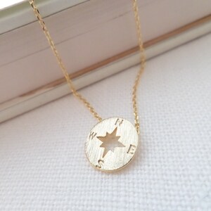 May include: A gold necklace with a compass pendant. The compass has a star in the center and the letters N, S, E, and W around the edge.