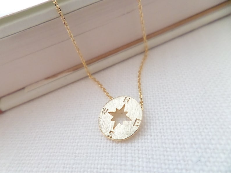 May include: A gold necklace with a compass pendant. The compass has a star in the center and the letters N, S, E, and W around the edge.