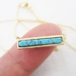 May include: A gold chain necklace with a turquoise bar pendant.