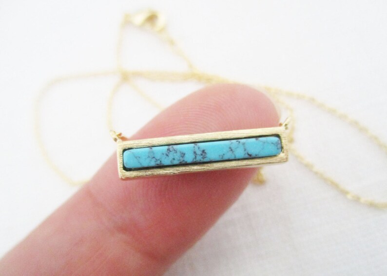 May include: A gold chain necklace with a turquoise bar pendant.