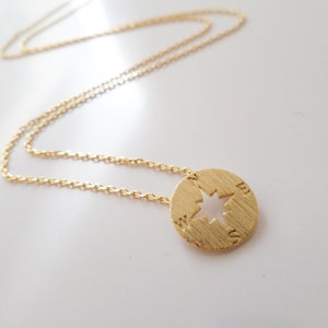 May include: A gold chain necklace with a compass pendant. The compass has a cut-out star design and the letters N, E, S, and W are engraved around the edge.