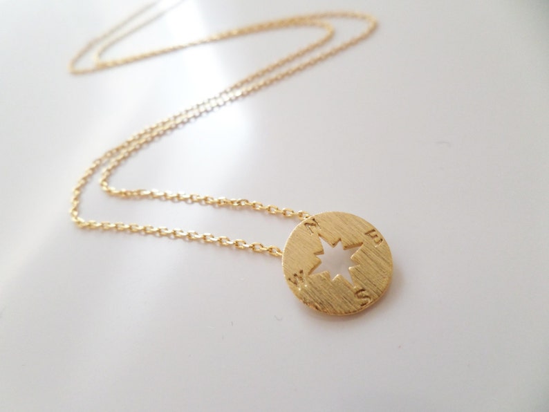May include: A gold chain necklace with a compass pendant. The compass has a cut-out star design and the letters N, E, S, and W are engraved around the edge.