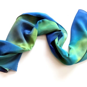 May include: A blue and green silk scarf with a gradient pattern. The scarf is folded and draped on a white background.