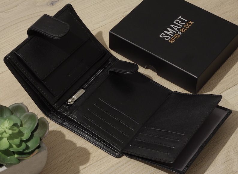 May include: A black leather wallet with a flap closure and multiple card slots. The wallet is open to reveal the interior, which has several compartments for cash and cards. The wallet is labeled "SMART RFID BLOCK".