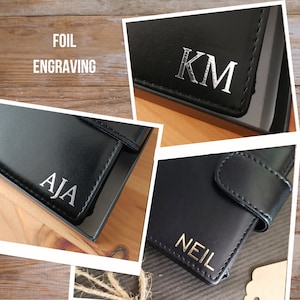May include: Three black leather wallets with foil engraving. The first wallet has the initials "KM" in silver foil. The second wallet has the name "AJA" in silver foil. The third wallet has the name "NEIL" in gold foil.