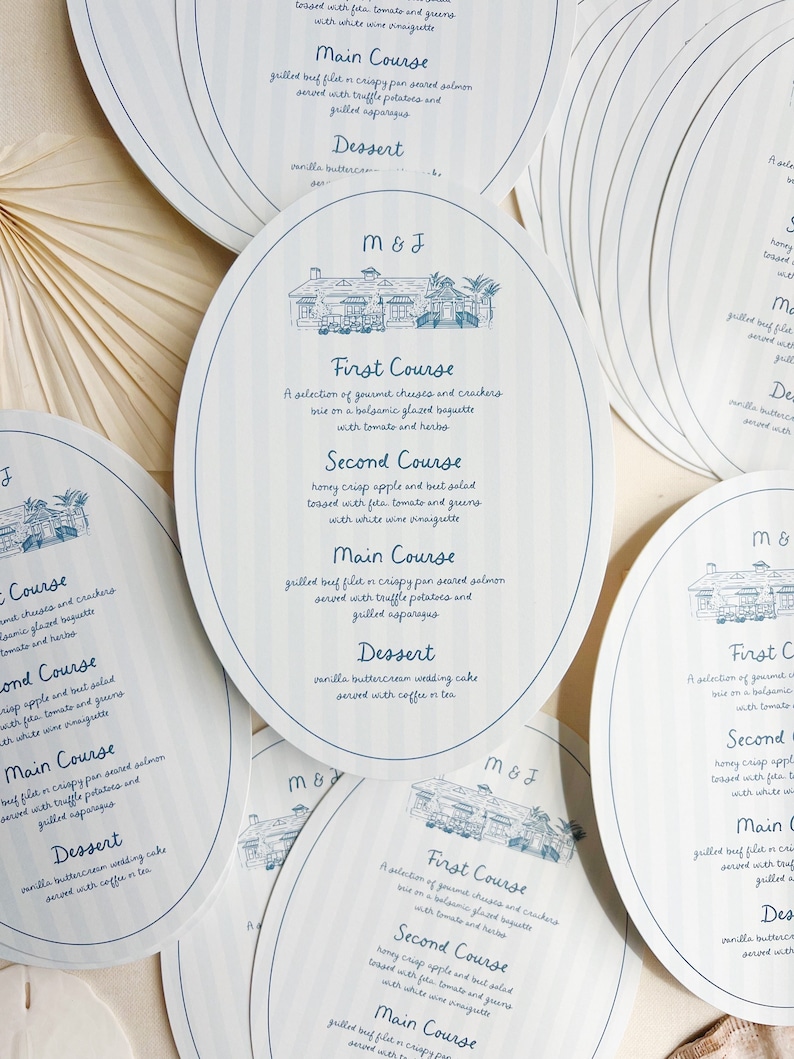 May include: A set of four blue and white oval-shaped wedding menu cards with a hand-drawn illustration of a building. The menu cards list the courses for the wedding reception: First Course, Second Course, Main Course, and Dessert. The text on the cards is in a handwritten font.