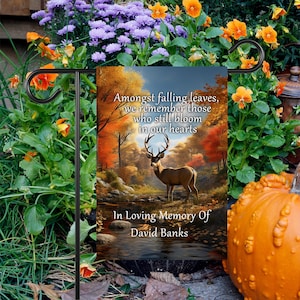 May include: A garden flag with a fall scene featuring a deer standing in a stream. The flag has the text "Amongst falling leaves, we remember those who still bloom in our hearts. In Loving Memory Of David Banks."