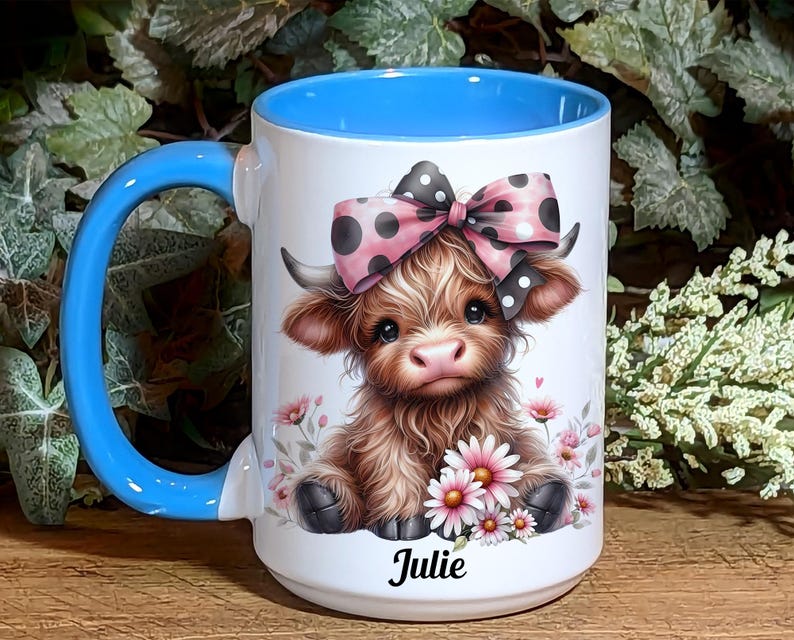 A beautifully designed personalized Highland Cow mug featuring an adorable brown cow with a pink and black polka dot bow, surrounded by soft pink flowers. This 15-ounce ceramic mug is available with a black, white, or blue handle.