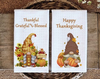May include: Two white kitchen towels with a gnome design. The first towel has a gnome with a brown hat and the text "Thankful Grateful and Blessed". The second towel has a gnome with a brown hat and the text "Happy Thanksgiving".