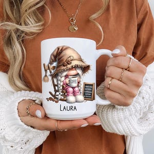 May include: White ceramic coffee mug with a gnome illustration. The gnome is wearing a brown hat and holding a coffee cup that says "Coffee". The mug has the text "I don't rise and shine I caffeinate and hope for the best" and the name "Laura" printed on it.