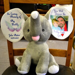 May include: A gray plush elephant toy with white ears. The left ear has text that reads "In Loving Memory of My Daddy John Michael 1976-2010" and a wing graphic. The right ear has a photo and text that reads "You Will Forever Be Daddy's Little Girl".
