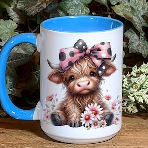 A beautifully designed personalized Highland Cow mug featuring an adorable brown cow with a pink and black polka dot bow, surrounded by soft pink flowers. This 15-ounce ceramic mug is available with a black, white, or blue handle.