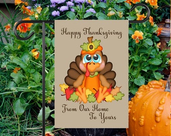 May include: A brown garden flag with a cartoon turkey wearing a pilgrim hat and surrounded by fall leaves. The text on the flag reads "Happy Thanksgiving From Our Home To Yours".