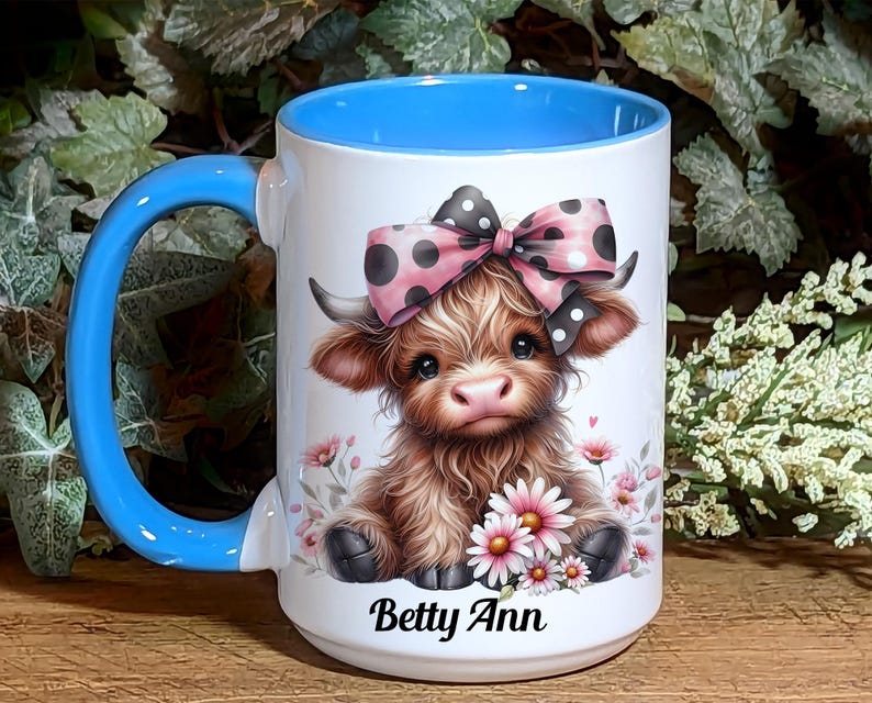 A beautifully designed personalized Highland Cow mug featuring an adorable brown cow with a pink and black polka dot bow, surrounded by soft pink flowers. This 15-ounce ceramic mug is available with a black, white, or blue handle.