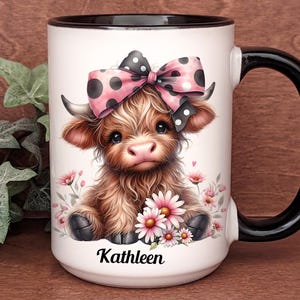 A beautifully designed personalized Highland Cow mug featuring an adorable brown cow with a pink and black polka dot bow, surrounded by soft pink flowers. This 15-ounce ceramic mug is available with a black, white, or blue handle.