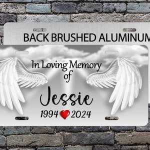 May include: A white brushed aluminum memorial plaque with a pair of white angel wings, the text "In Loving Memory of Jessie 1994 2024" and a red heart.